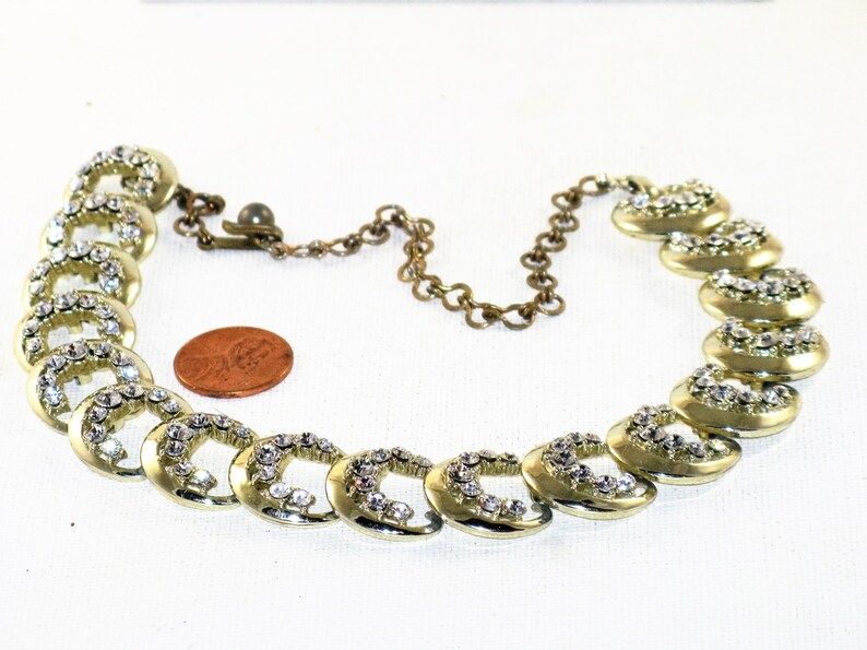 May include: A gold tone necklace with a chain and a series of linked, crescent-shaped charms set with clear rhinestones.