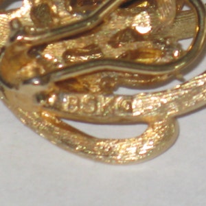 May include: Gold-toned metal earring with a swirl design and a clasp closure. The earring is marked "BSK 10".