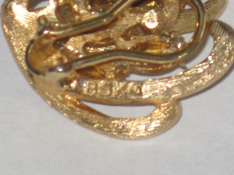 May include: Gold-toned metal earring with a swirl design and a clasp closure. The earring is marked "BSK 10".