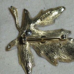 May include: Gold-tone leaf-shaped brooch with a pin and catch on the back. The brooch has a textured surface and the word "INO" is stamped on the back.