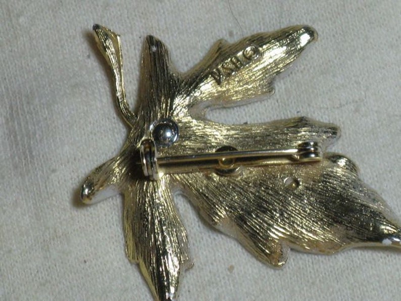May include: Gold-tone leaf-shaped brooch with a pin and catch on the back. The brooch has a textured surface and the word "INO" is stamped on the back.