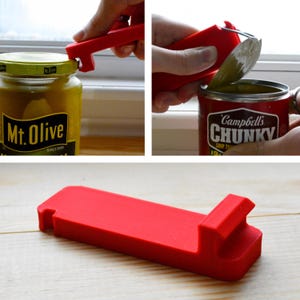 May include: A red, multi-purpose kitchen tool is shown in use, opening a jar of Mt. Olive pickles and a can of Campbell's Chunky soup. The tool is made of a solid, durable material and is designed for easy grip and leverage.