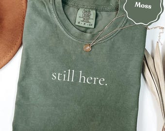 Still here t-shirt, motivational quote tee, resilience statement shirt, inspiring message t-shirt, minimalist text apparel, strong spirit