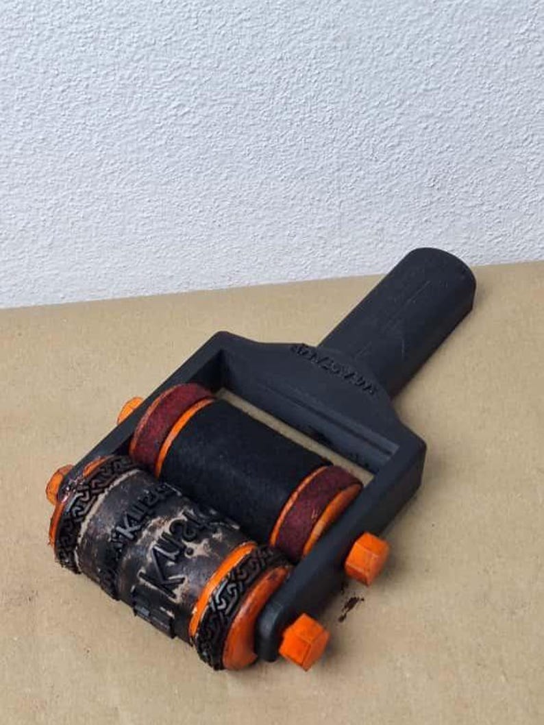 K&ouml;nnte beinhalten: Eine schwarz-orange Stempelrolle mit zwei zylindrischen Rollen. Eine Rolle hat das Wort "Kiri" in einer dekorativen Schriftart. Die andere Rolle ist schwarz mit roten Akzenten. Der Griff ist schwarz mit dem Text "2020 AW".