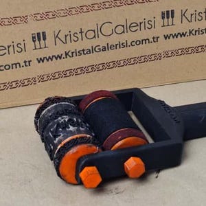 K&ouml;nnte beinhalten: Ein schwarz-oranges Dekorationsobjekt mit zwei zylindrischen Komponenten. Eine ist schwarz mit orangefarbenen Akzenten, die andere ist schwarz mit roter Oberseite. Das Objekt hat einen schwarzen Griff und orangefarbene sechseckige Details.