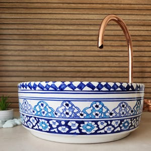 Peut inclure: Un évier en céramique blanc avec un motif floral bleu et blanc. L'évier a un bord décoratif et un robinet en cuivre. L'évier est de forme ronde et repose sur une surface de couleur claire.