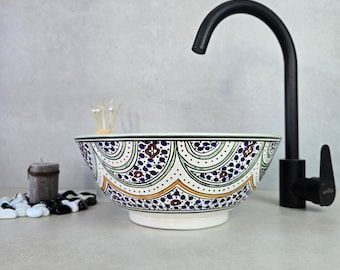 Può includere: Una ciotola in ceramica bianca con un motivo geometrico blu, verde e giallo. La ciotola è un lavabo da bagno e viene abbinata a un rubinetto nero.