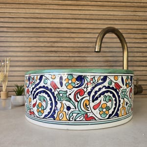 May include: A white ceramic sink with a green rim and a colorful floral pattern. The sink is decorated with blue, red, yellow, and green swirls and flowers.