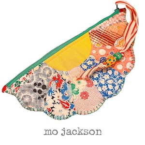 May include: A handmade, patchwork zippered pouch with a scalloped edge. The pouch features a variety of floral and geometric patterned fabrics in shades of red, blue, yellow, and white. A green zipper and a striped ribbon handle complete the design. The text "mo jackson" is at the bottom.