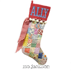 May include: A Christmas stocking featuring a red cuff with the name ALLY in blue letters, a patchwork body made of various colorful floral and patterned fabric squares, a red and white gingham ribbon bow, and a row of small white pom-poms.
