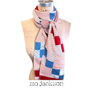 May include: A patchwork scarf with red, white, and blue squares and floral patterns. The scarf is draped over a mannequin. The text "mo jackson" is at the bottom.