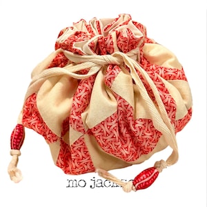 May include: A cream-colored drawstring bag with red patterned accents. The bag features a repeating geometric design in red and cream, with a drawstring closure and decorative red beads on the ends. The text "mo jack" is printed on the bottom.
