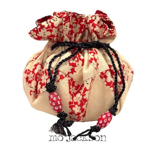 May include: A drawstring pouch with a cream-colored background and red floral pattern. The pouch has a black drawstring with red and white beaded accents and black tassels. The text "mo jackson" is at the bottom.