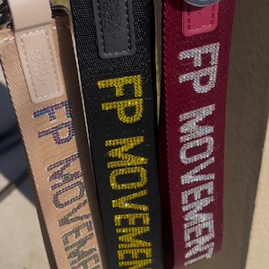 Pu&ograve; includere: Tre portachiavi in tessuto nero, bordeaux e beige con anelli argentati. Ogni portachiavi presenta il testo "FP MOVEMENT" in strass.