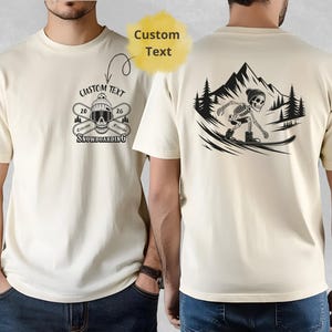 Op de afbeelding: Crèmekleurig T-shirt met een zwart grafisch ontwerp. De voorkant heeft een schedel met gekruiste ski's en de tekst "Custom Text", "Extreme Freeride Snowboarding". De achterkant toont een snowboardend skelet.