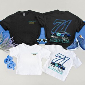 May include: A collection of black and white t-shirts featuring racing-themed graphics. The shirts display the number 71, a race car, and the name "Michael McDowell." Accessories include blue sneakers, sunglasses, and baby shoes.