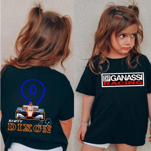 May include: Black t-shirts featuring racing-themed graphics. One shirt displays "CHIP GANASSI RACING" in a white box with red text. The other shirt has a blue number 9, a race car illustration, and "SCOTT DIXON" in orange.