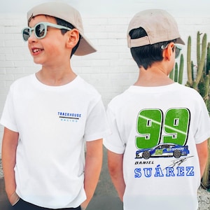 May include: White t-shirt with "TRACKHOUSE RACING" text on the front and a large "99" graphic on the back, along with a race car design and the name "DANIEL SUÁREZ". The shirt is worn by a child.
