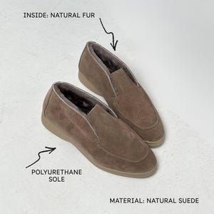 May include: A pair of taupe slip-on shoes crafted from natural suede. The shoes feature a natural fur lining on the inside and a polyurethane sole. Text on the image indicates the materials as natural suede, natural fur, and polyurethane sole.
