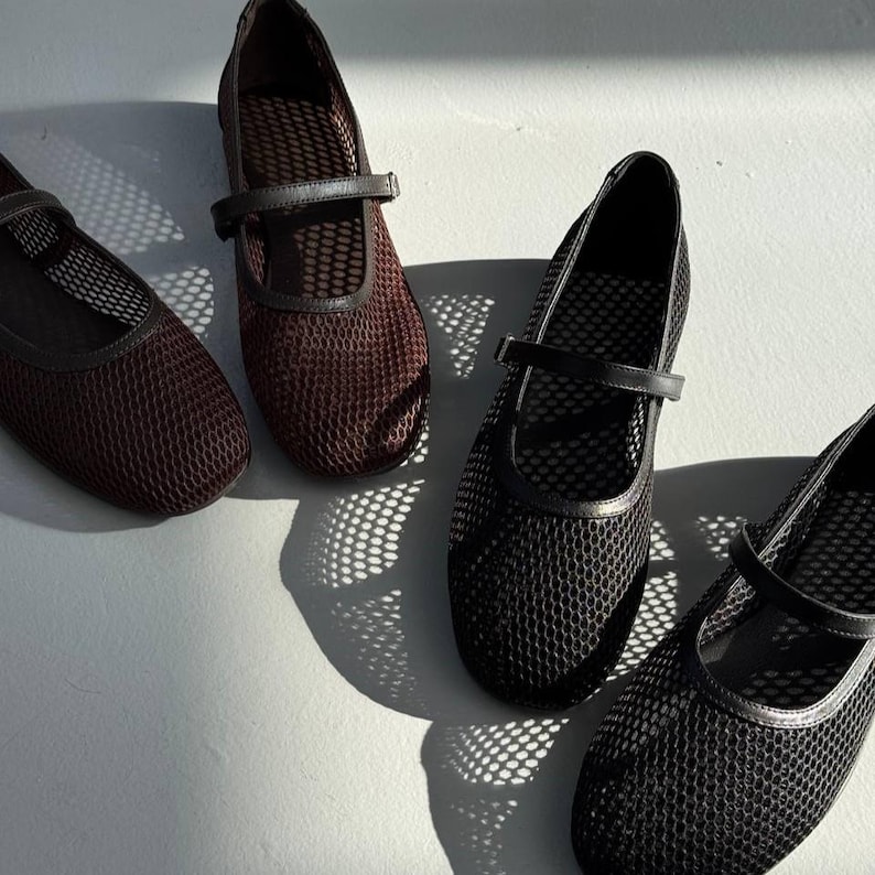 May include: Four Mary Jane style shoes featuring a mesh upper construction. Two shoes are dark brown and two are black. Each shoe has a thin strap across the instep with a buckle closure and a rounded toe design, showcasing a textured grid pattern.