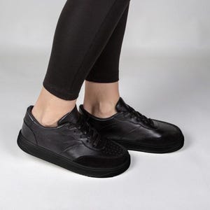 A person wearing black leggings and black sneakers is standing on a white background.