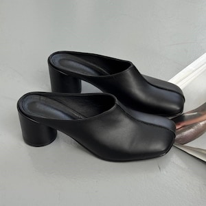 May include: A pair of black leather mules with a square toe and a block heel. The heels are approximately 3 inches high. The shoes are displayed on a light gray surface.