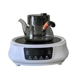 May include: A clear glass teapot with a black lid and handle, resting on a white base with a digital display. The base has buttons labeled "Timing", "Keep Warm", "Heat Water", "Make Tea", "Power", and "On/Off".