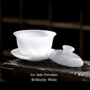 May include: A white porcelain tea bowl with a matching saucer and a separate lid featuring a small knob handle. The surface is smooth and glossy. The text Ice Jade Porcelain Brilliantly White is printed in white on the dark base below the tea set.