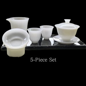 May include: A white 5-piece tea set, including a pitcher, two small cups, a gaiwan with saucer, and a tea strainer. The set is arranged on a dark, rectangular tray. The text "5-Piece Set" is displayed below the tea set.
