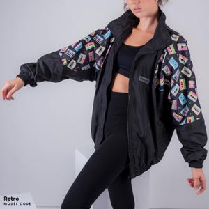May include: A black windbreaker jacket with a colorful cassette tape print on the sleeves. The jacket has a zipper closure and a stand-up collar.