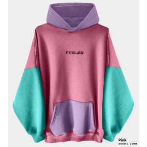 Può includere: Una felpa con cappuccio rosa, verde e viola con una grande tasca sul davanti. La felpa ha la scritta "VTKLAWN" stampata sul davanti.