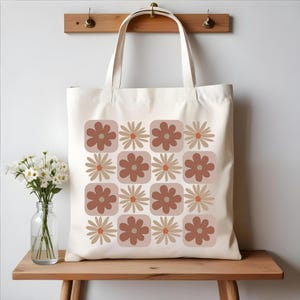 May include: A white canvas tote bag with a brown and beige floral pattern. The flowers are arranged in a grid pattern and have a retro style.