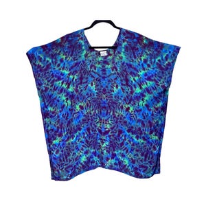May include: A short-sleeved poncho top featuring a vibrant tie-dye pattern in shades of deep purple, royal blue, and bright turquoise. The garment has a wide, loose-fitting silhouette with a rounded neckline and is displayed on a black hanger.