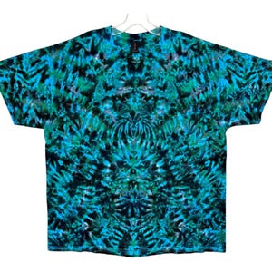 May include: A short-sleeved t-shirt with a vibrant tie-dye pattern in shades of teal, turquoise, and black. The shirt is hanging on a white hanger against a white background. The tie-dye design is symmetrical, creating a visually striking effect.