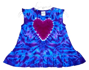 May include: A tie-dye baby dress with a pink heart design. The dress has a ruffled hem and is made of a soft, comfortable fabric.