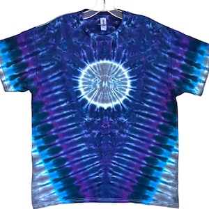 May include: A tie-dye t-shirt with a circular pattern in shades of blue, purple, and gray. The shirt has a white center with a darker blue ring around it.