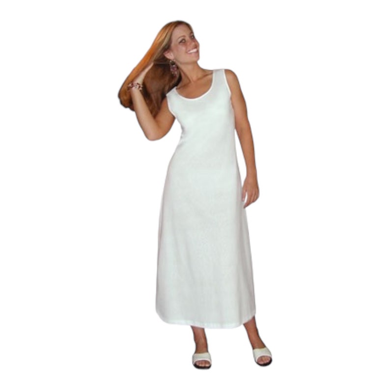 May include: A sleeveless, floor-length white dress with a scoop neckline. The dress has a simple, elegant design and is made of a lightweight fabric. The model is wearing white sandals.