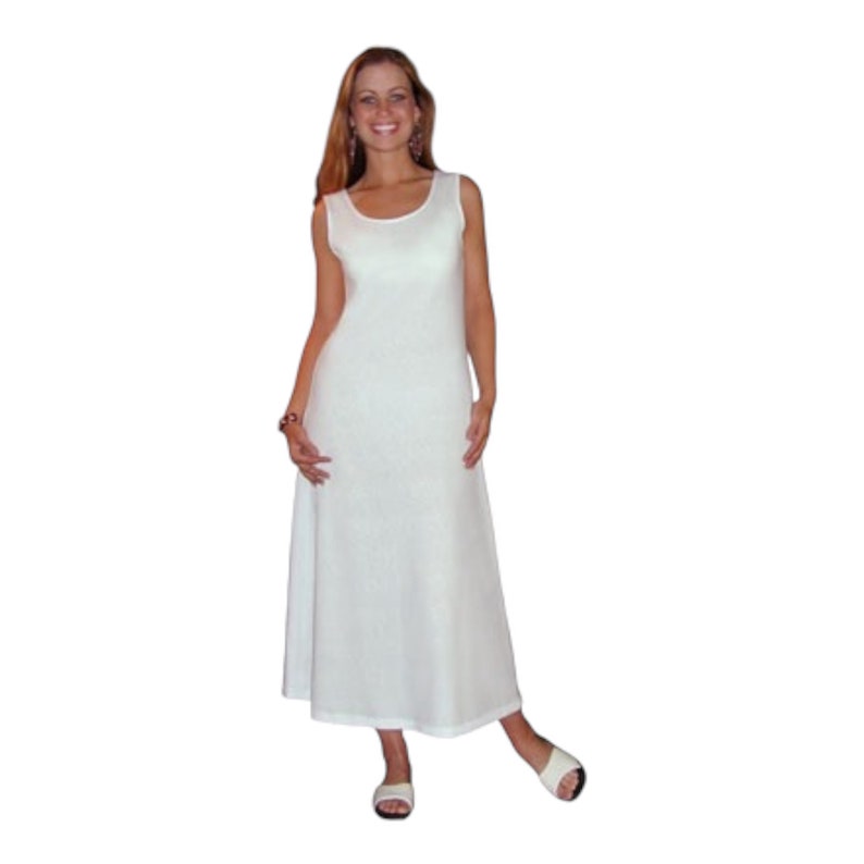 May include: A sleeveless, white maxi dress with a scoop neckline. The dress has a flowing, A-line silhouette and is paired with white sandals. The fabric appears to have a subtle texture. The model is smiling.