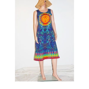 May include: A sleeveless tie-dye dress in shades of blue, green, yellow, orange, and red. The dress features a sunburst design on the chest and a rainbow-striped hem. A straw hat is on the mannequin's head.