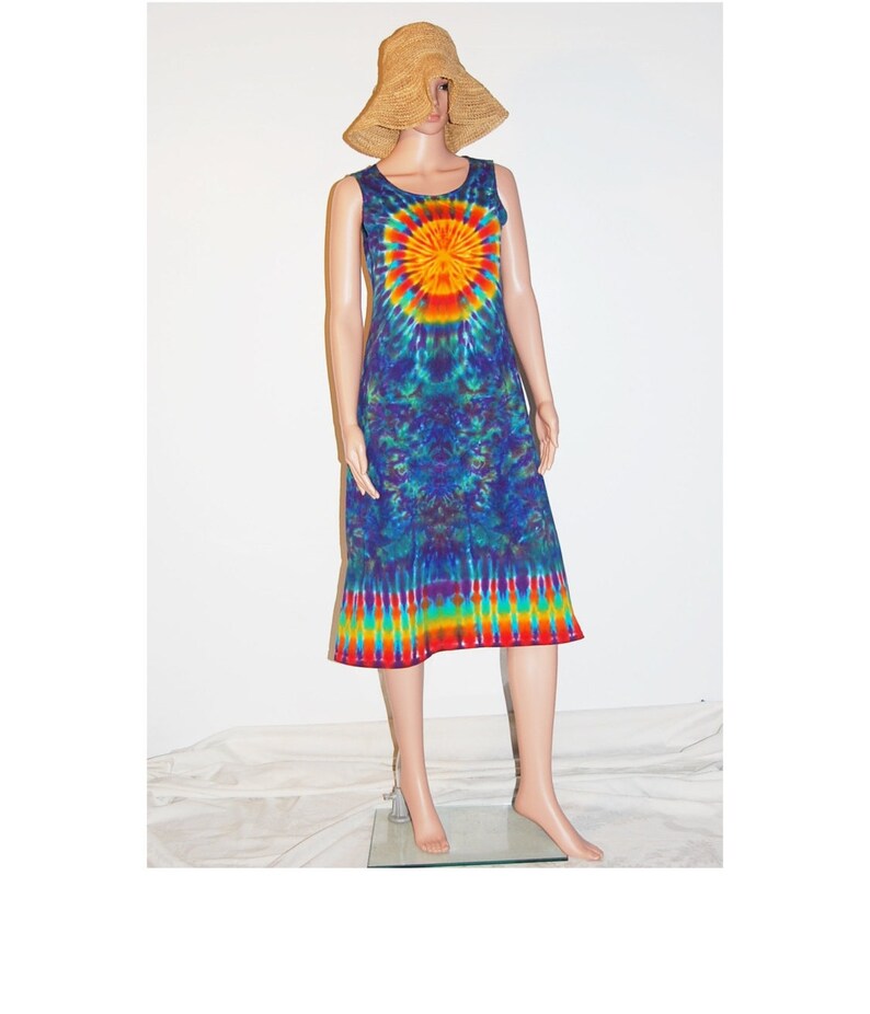 May include: A sleeveless tie-dye dress in shades of blue, green, yellow, orange, and red. The dress features a sunburst design on the chest and a rainbow-striped hem. A straw hat is on the mannequin's head.