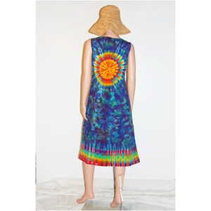 May include: A sleeveless tie-dye dress with a vibrant sunburst design on the back, transitioning to a rainbow hem. The dress is displayed on a mannequin, paired with a straw sun hat. The dress is a knee-length style.