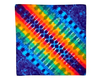 Può includere: Un bandana tie-dye colorato con un motivo arcobaleno e uno sfondo blu. Il bandana è in cotone ed è perfetto per aggiungere un tocco di colore a qualsiasi outfit.