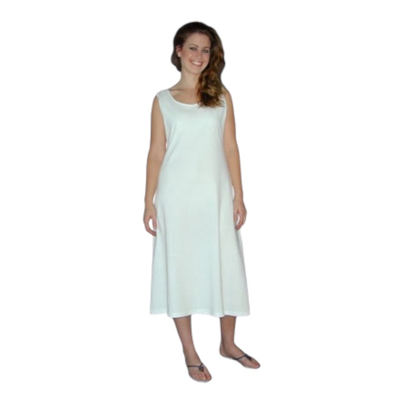 May include: A sleeveless, off-white dress with a scoop neckline. The dress falls to mid-calf and has a slightly flared skirt. The woman in the image is wearing the dress and sandals.