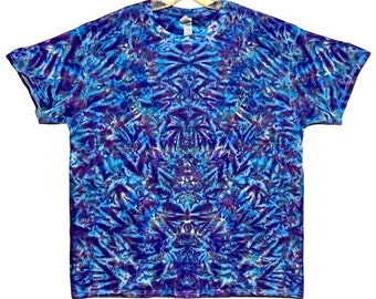Op de afbeelding: Een tie-dye T-shirt met een blauwe, paarse en witte kleurstelling. Het shirt heeft een symmetrisch patroon met een centraal punt.