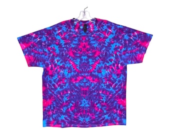 Op de afbeelding: Een tie-dye T-shirt met een levendig roze, blauw en paars kleurenschema. Het shirt heeft een symmetrisch patroon met een draaiende vorm.