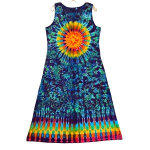 May include: A sleeveless tie-dye dress in a vibrant array of colors. The dress features a central sunburst design in yellow, orange, and red, surrounded by a blue and green pattern. The bottom hem has a rainbow stripe design.