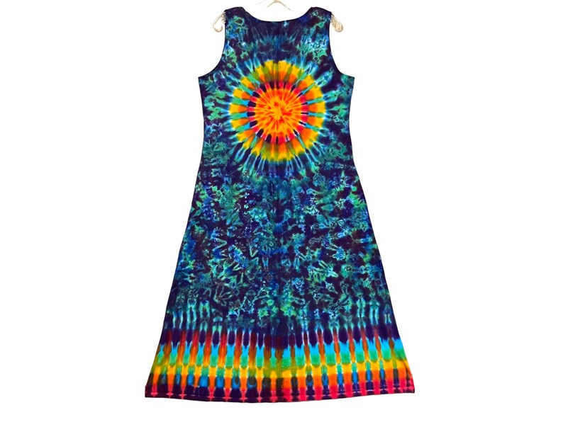 May include: A sleeveless tie-dye dress in a vibrant array of colors. The dress features a central sunburst design in yellow, orange, and red, surrounded by a blue and green pattern. The bottom hem has a rainbow stripe design.