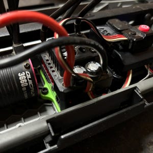 May include: A close-up of a black and green electric motor with the text "QUICRUN 3660 3150KV" printed on the side. The motor is mounted in a black and gray chassis with red and white wires.