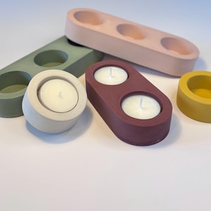May include: Set of four tealight candle holders in various colours, including pink, green, brown, and yellow. The holders are made of concrete and have a smooth, matte finish.