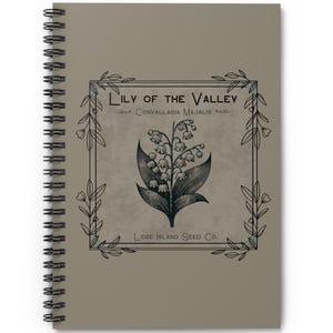 May include: A spiral bound notebook with a vintage illustration of a lily of the valley flower. The illustration is in black and white and is surrounded by a decorative frame. The text "Lily of the Valley" and "Convallaria Majalis" is printed in black on a beige background. The text "Lode Island Seed Co." is printed at the bottom of the illustration.